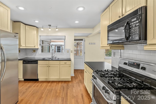 kitchen with cream cabinetry, appliances with stainless steel finishes, decorative backsplash, sink, and light hardwood / wood-style flooring