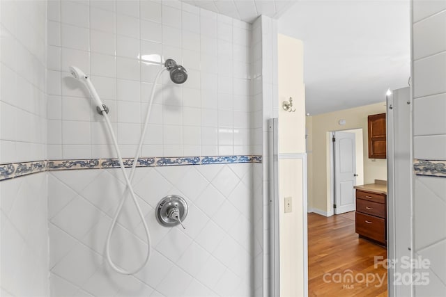 bathroom with a tile shower, vanity, and wood-type flooring