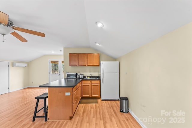 kitchen with white fridge, vaulted ceiling, a kitchen bar, light hardwood / wood-style floors, and a wall unit AC