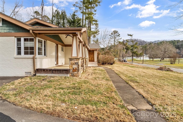 view of side of home featuring a porch, a lawn, and ceiling fan