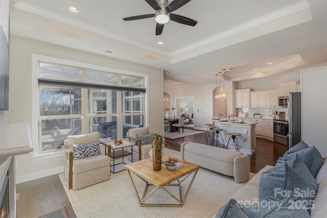 living room with light hardwood / wood-style floors, crown molding, a raised ceiling, and ceiling fan