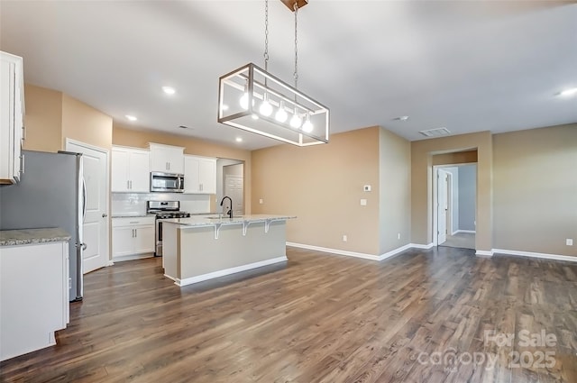 kitchen with pendant lighting, appliances with stainless steel finishes, dark wood-type flooring, white cabinetry, and a center island with sink