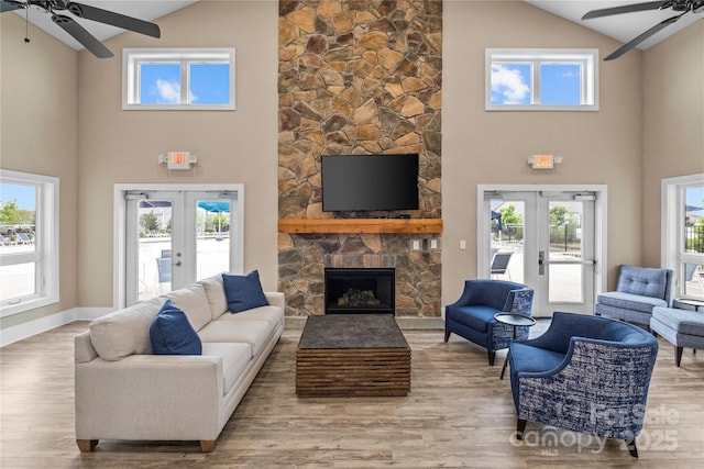 living room with ceiling fan, french doors, a stone fireplace, and light hardwood / wood-style floors