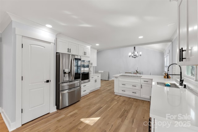 kitchen with white cabinets, appliances with stainless steel finishes, decorative light fixtures, sink, and light wood-type flooring