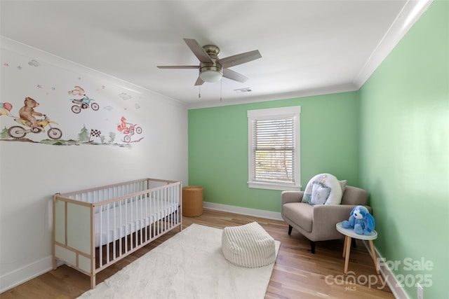 bedroom featuring ceiling fan, a crib, ornamental molding, and light hardwood / wood-style flooring