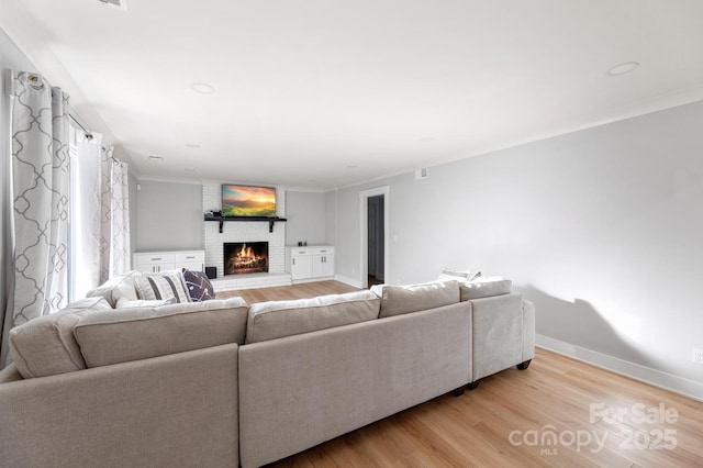 living room with light hardwood / wood-style floors, crown molding, and a brick fireplace