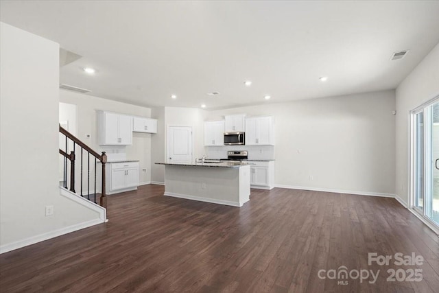 kitchen featuring dark hardwood / wood-style floors, stainless steel appliances, a kitchen island with sink, white cabinets, and stone counters