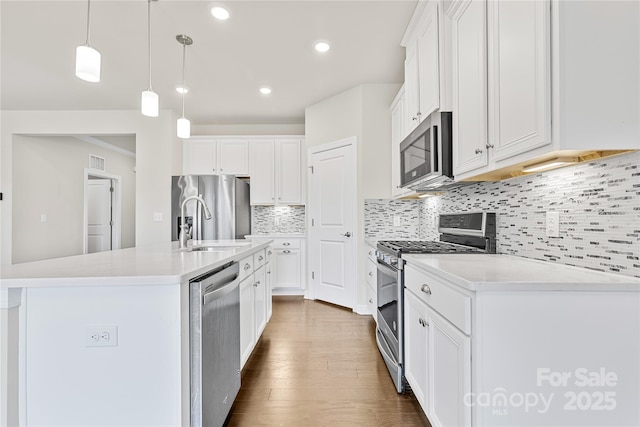 kitchen featuring decorative light fixtures, white cabinets, appliances with stainless steel finishes, and a kitchen island with sink