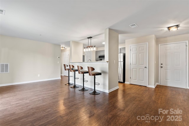 kitchen with dark hardwood / wood-style floors, a kitchen bar, stainless steel fridge, and kitchen peninsula