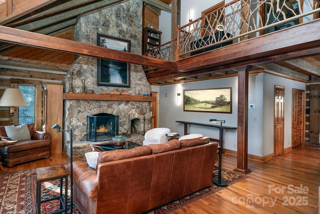 living room featuring a towering ceiling, a stone fireplace, and hardwood / wood-style floors