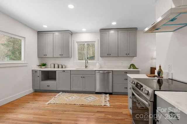 kitchen featuring appliances with stainless steel finishes, wall chimney range hood, light hardwood / wood-style floors, sink, and gray cabinets