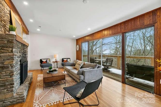 living room featuring light wood-type flooring, wood walls, and a stone fireplace