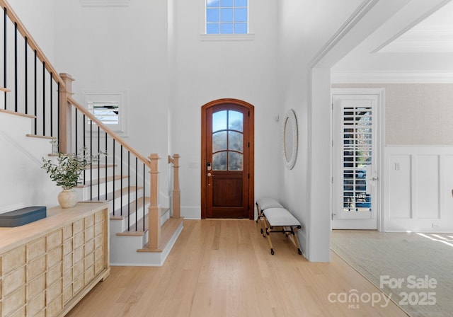 foyer featuring a high ceiling, light wood-type flooring, and crown molding