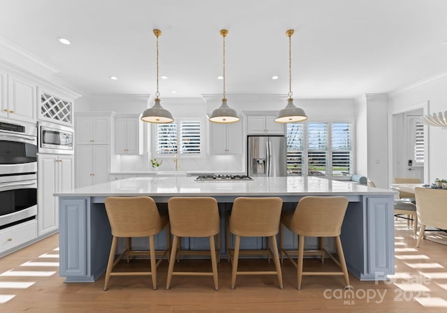 kitchen with stainless steel appliances, white cabinets, hanging light fixtures, and a spacious island