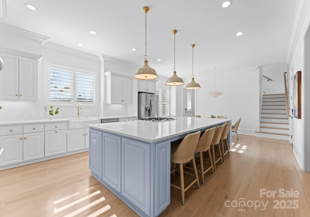 kitchen with a center island, white cabinetry, light hardwood / wood-style floors, pendant lighting, and appliances with stainless steel finishes