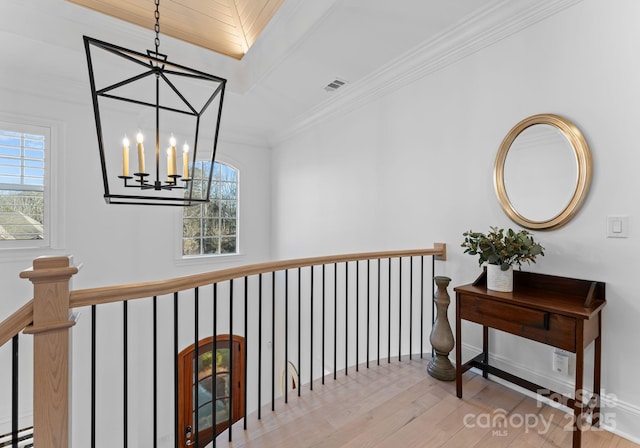 hallway with an inviting chandelier, ornamental molding, plenty of natural light, and light hardwood / wood-style flooring