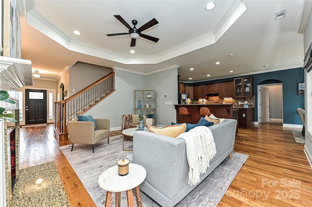 living room featuring dark hardwood / wood-style floors, ceiling fan, a tray ceiling, and crown molding