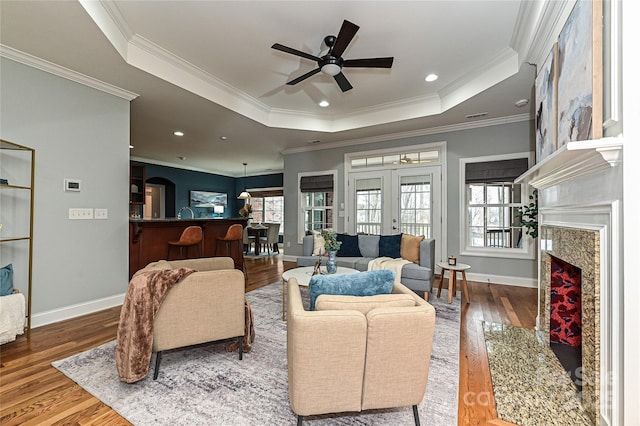 living room featuring hardwood / wood-style floors, a tray ceiling, a high end fireplace, and french doors