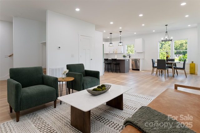 living room with sink, a notable chandelier, and light wood-type flooring