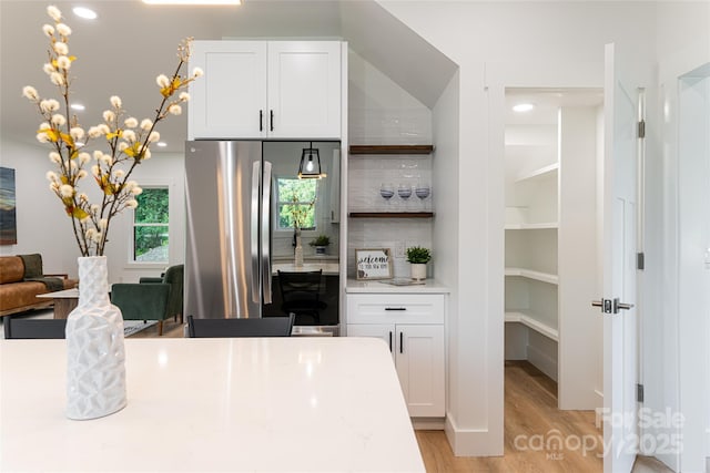 kitchen featuring white cabinetry, stainless steel fridge, light stone countertops, and light wood-type flooring