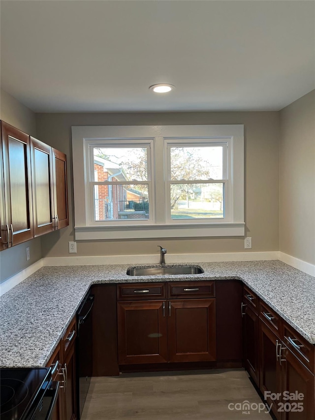 kitchen with sink, black dishwasher, light hardwood / wood-style floors, dark brown cabinets, and light stone countertops