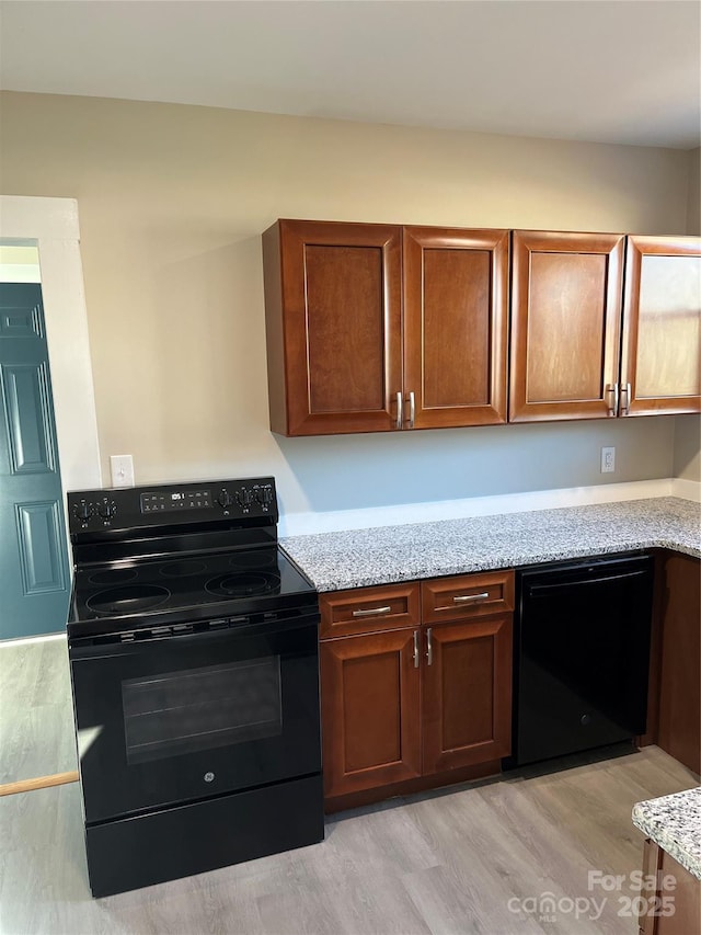 kitchen featuring light stone countertops, light wood-type flooring, and black appliances