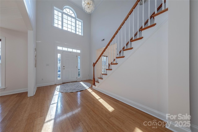 entrance foyer featuring wood-type flooring, a towering ceiling, and a notable chandelier