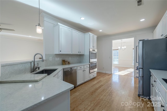 kitchen with appliances with stainless steel finishes, sink, white cabinets, and decorative light fixtures