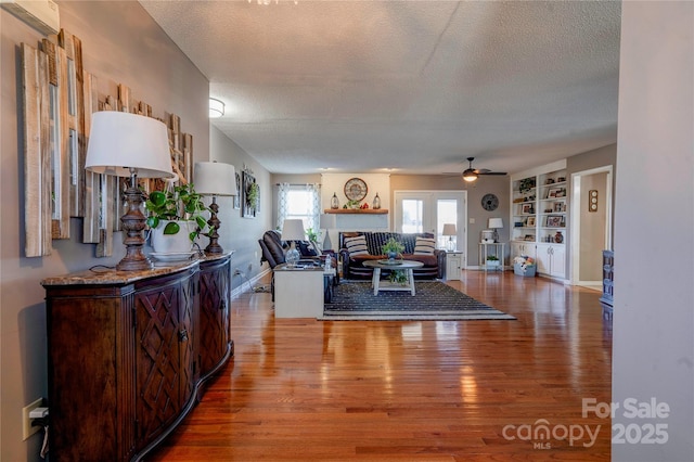 living room with hardwood / wood-style floors, built in shelves, a textured ceiling, and a brick fireplace