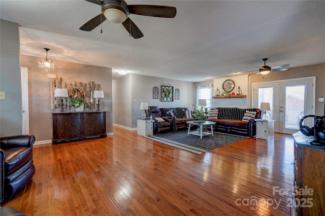 living room featuring french doors, ceiling fan, wood-type flooring, and a textured ceiling