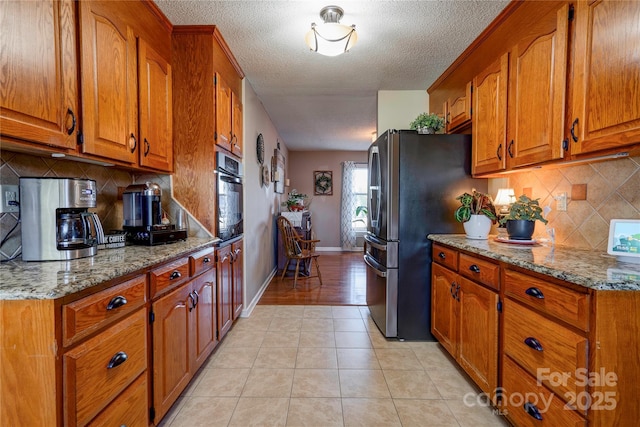 kitchen featuring light tile patterned flooring, stainless steel refrigerator, tasteful backsplash, light stone counters, and wall oven