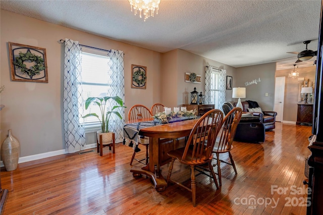 dining area featuring ceiling fan with notable chandelier, wood-type flooring, and a textured ceiling