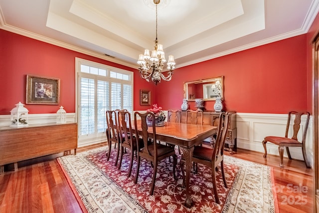 dining area with a notable chandelier, hardwood / wood-style floors, crown molding, and a tray ceiling