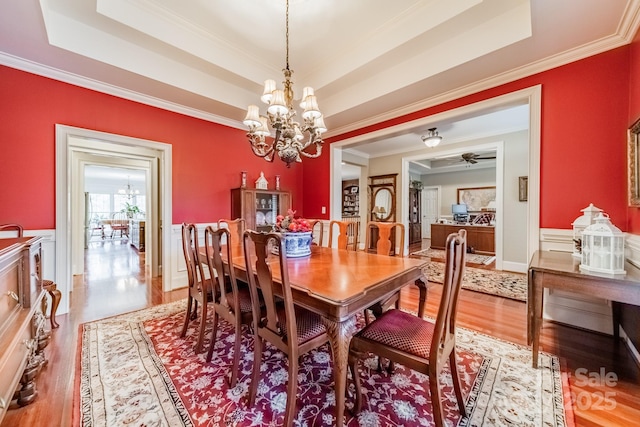 dining area featuring ceiling fan with notable chandelier, hardwood / wood-style floors, a tray ceiling, and ornamental molding