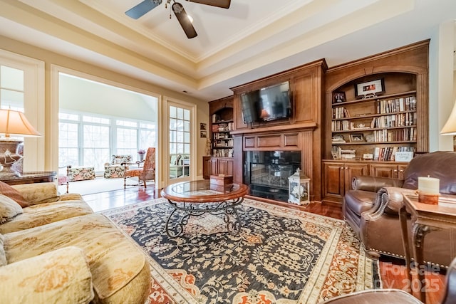 living room with hardwood / wood-style floors, a tray ceiling, crown molding, built in features, and ceiling fan