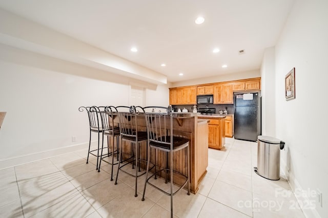 kitchen featuring a kitchen breakfast bar, a kitchen island with sink, backsplash, black appliances, and light tile patterned flooring