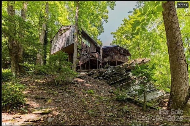 rear view of property with stairs, a wooden deck, and a view of trees