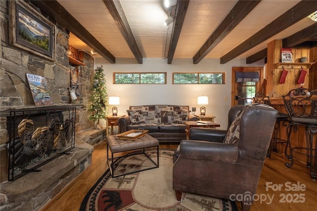 living room with beam ceiling, a stone fireplace, and wood finished floors