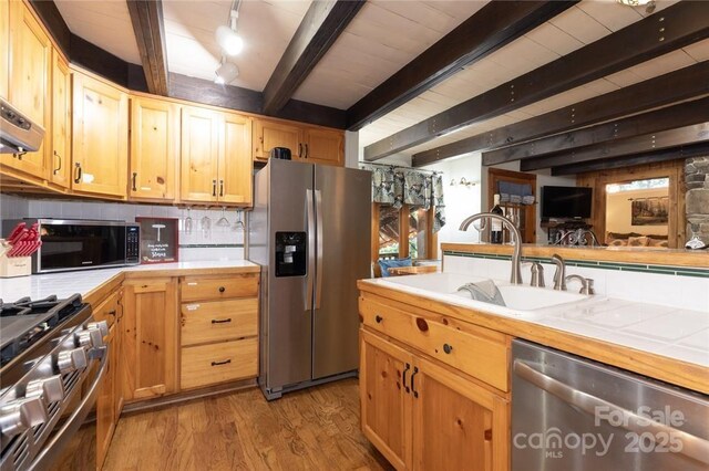 kitchen featuring tile countertops, stainless steel appliances, decorative backsplash, a sink, and wood finished floors