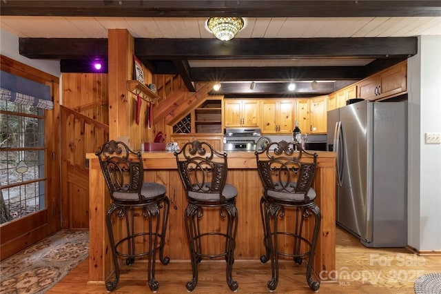 kitchen featuring a peninsula, a kitchen breakfast bar, light wood-type flooring, freestanding refrigerator, and beamed ceiling