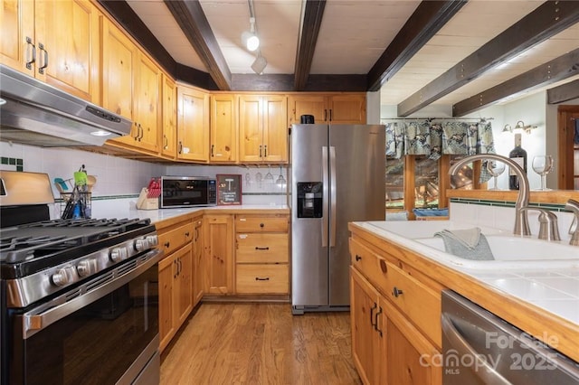 kitchen featuring beam ceiling, stainless steel appliances, decorative backsplash, light wood-type flooring, and under cabinet range hood