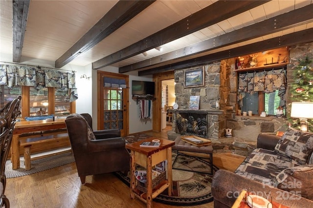 sitting room with a stone fireplace, wood finished floors, and beam ceiling