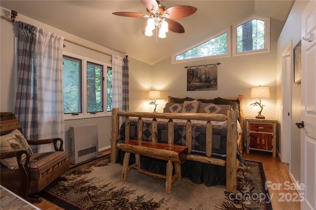 bedroom with heating unit, vaulted ceiling, and wood finished floors