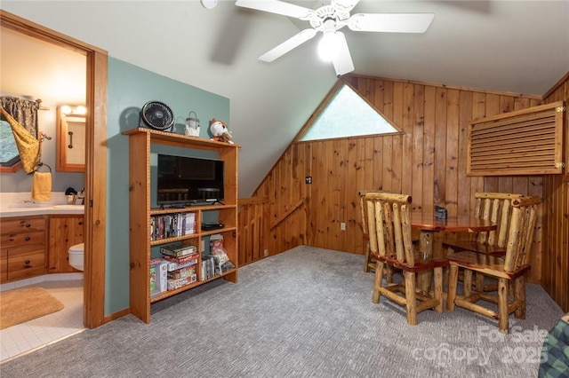 living area with carpet, a ceiling fan, vaulted ceiling, wooden walls, and an upstairs landing