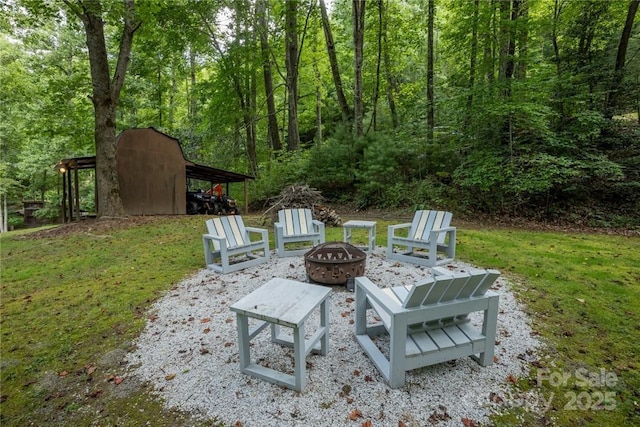 view of patio / terrace with a forest view, an outdoor fire pit, a storage unit, and an outdoor structure