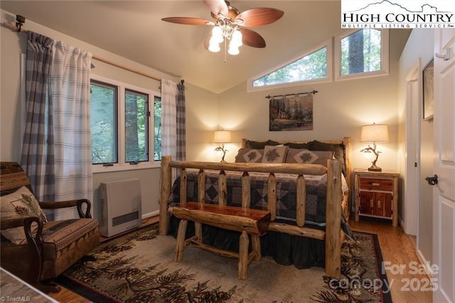 bedroom with vaulted ceiling, multiple windows, wood finished floors, and heating unit