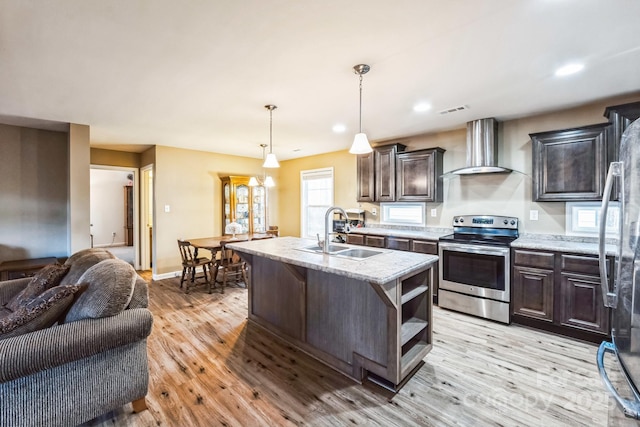 kitchen featuring a kitchen island with sink, appliances with stainless steel finishes, hanging light fixtures, sink, and wall chimney range hood