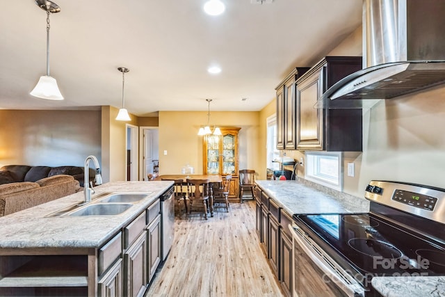 kitchen with a kitchen island with sink, stainless steel appliances, hanging light fixtures, wall chimney exhaust hood, and sink