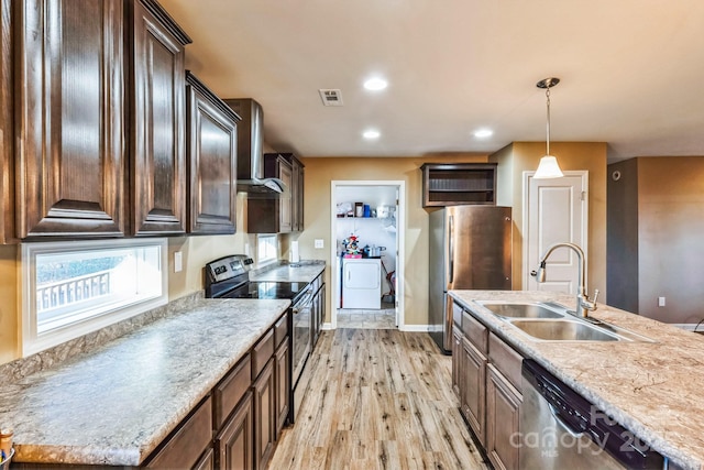 kitchen with stainless steel appliances, sink, hanging light fixtures, washer / dryer, and wall chimney range hood