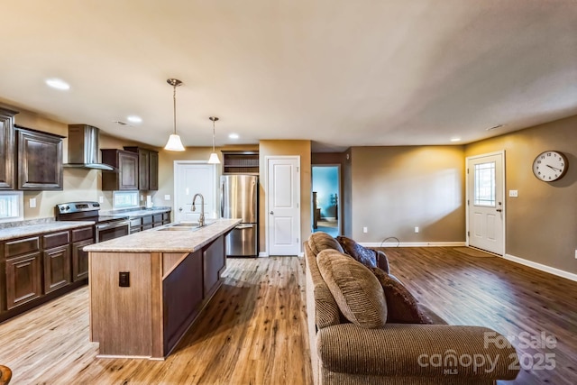 kitchen featuring sink, wall chimney exhaust hood, hanging light fixtures, a center island with sink, and appliances with stainless steel finishes